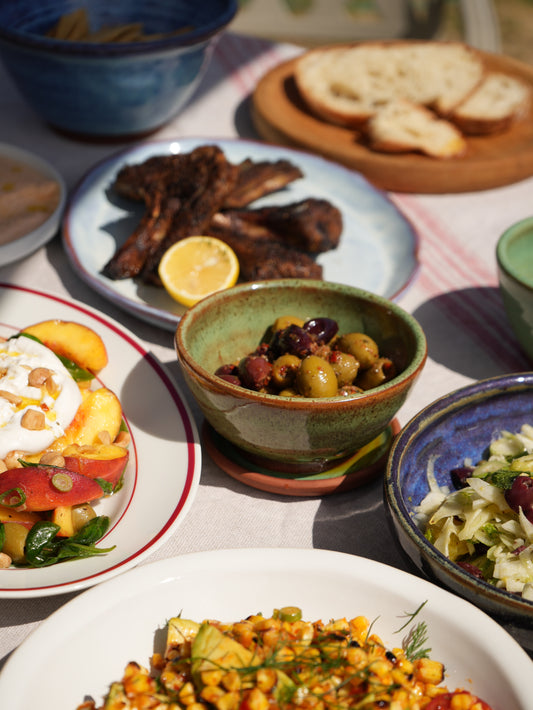 Olive bowl with grilled meat, salads and bread on a sharing table