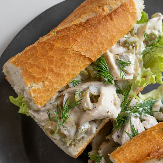 Mediterranean chicken sandwich filled with sliced chicken breast, olives, cornichons, lettuce and herbs on crusty sourdough.