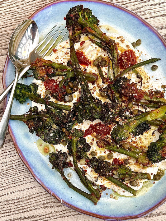 Charred purple sprouting broccoli served over a swirl of spicy harissa labneh, garnished with capers and dukkah