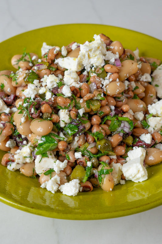 Mixed beans and feta salad with olives, capers, and fresh herbs in a serving bowl