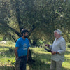 Two men standing outdoors, one holding a tablet, with trees in the background