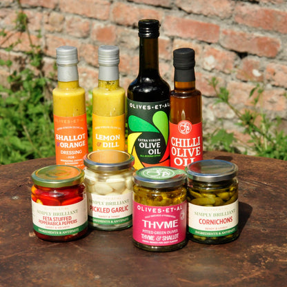 Assorted condiments including bottles and jars on a wooden surface with a brick wall background.