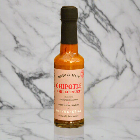 Bottle of Raw & Hot Chipotle Chilli Sauce on a wooden surface with a blurred background