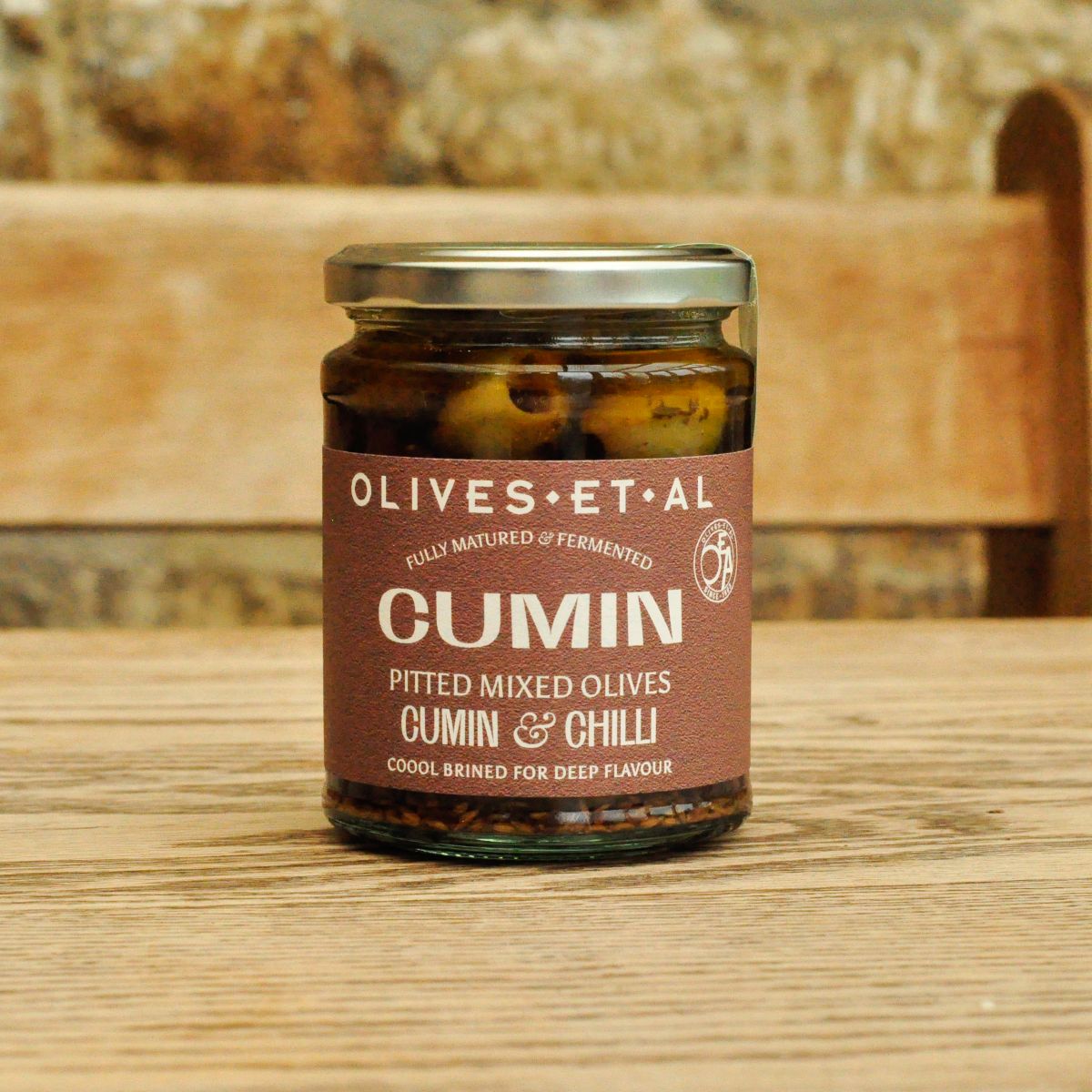 Jar of Olives et al Cumin Pitted Mixed Olives on a wooden surface with a stone wall background
