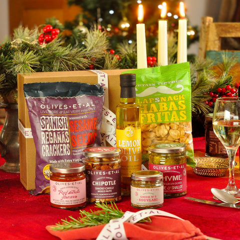 Gourmet gift basket with snacks and oils on a festive table with candles and Christmas decorations.