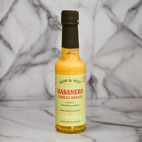 Bottle of Raw & Hot Habanero Chilli Sauce on a marble background with a blurred background