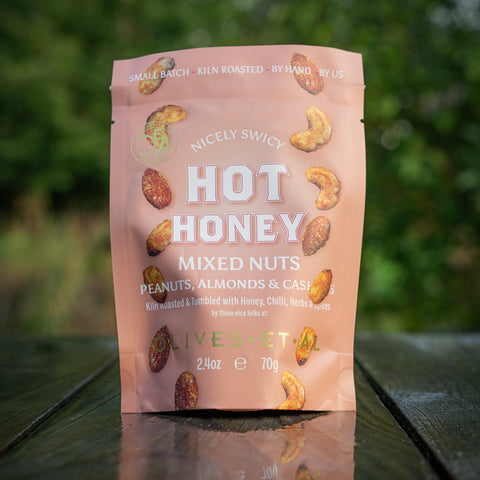 Package of Nicely Swicy Hot Honey Mixed Nuts on a wooden surface with a blurred green background