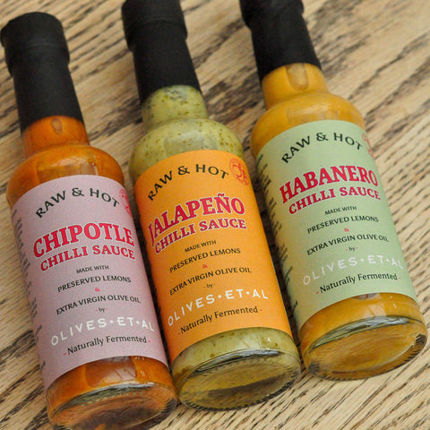 Three bottles of Raw & Hot chili sauces on a wooden surface