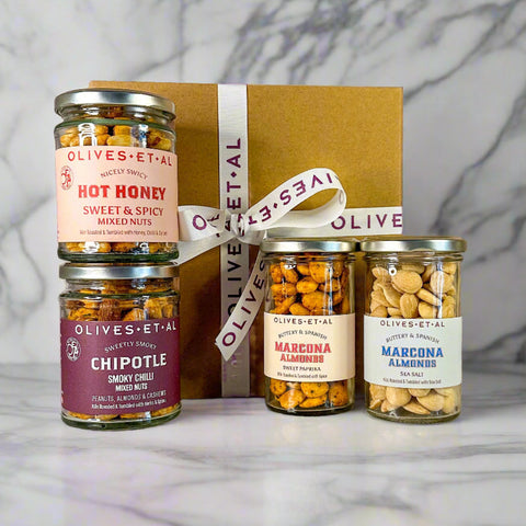 Jars of Olives & Et Al mixed nuts with a decorative box on a marble surface.