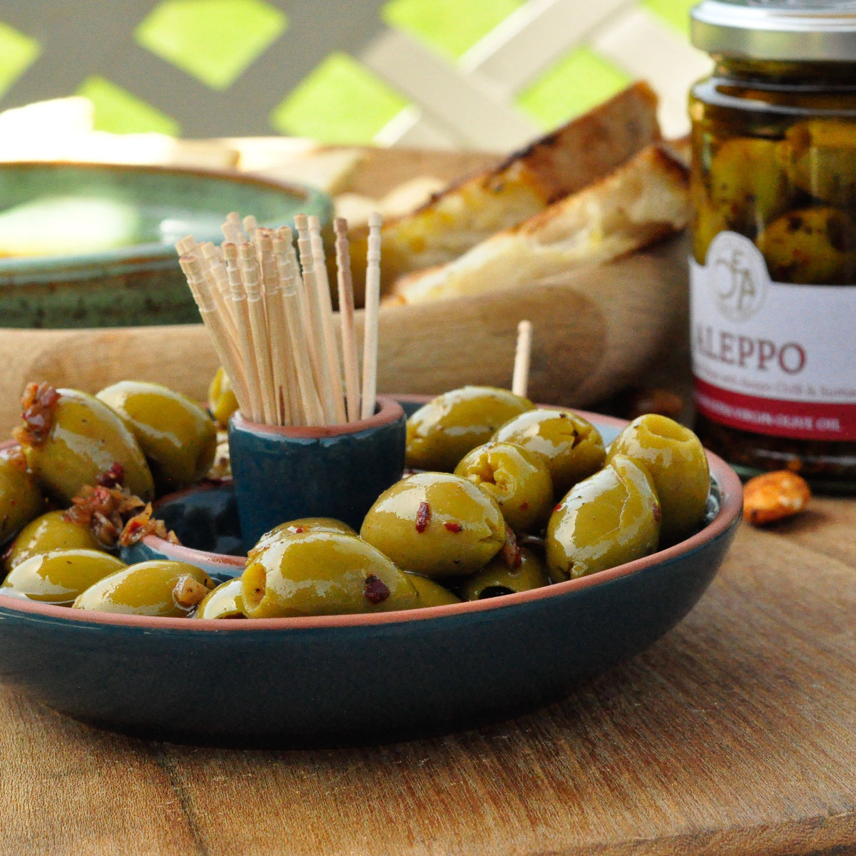 Bowl of olives with a jar of olives labeled 'Aleppo' on a wooden surface.