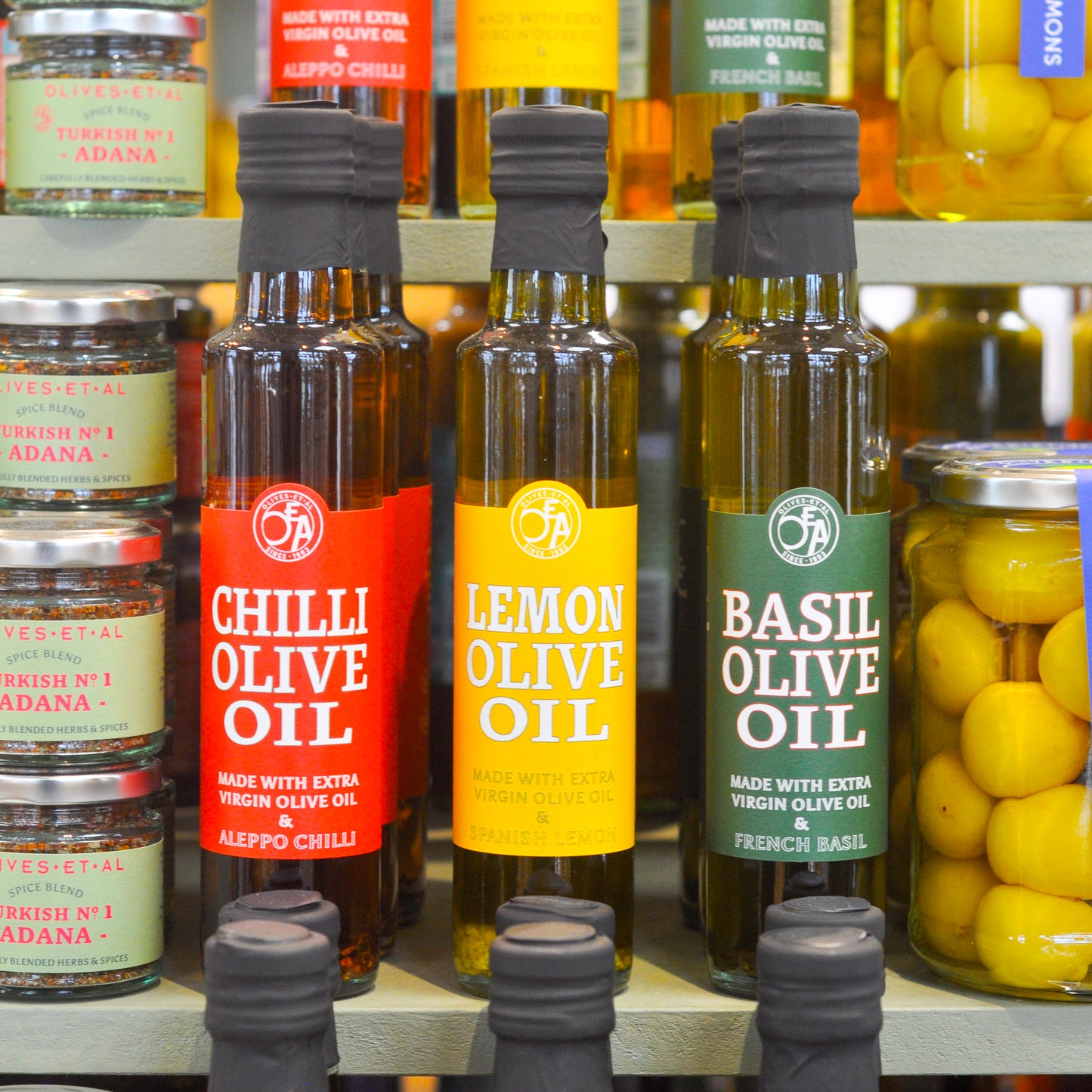 Bottles of olive oil with labels for Chilli, Lemon, and Basil on a store shelf.