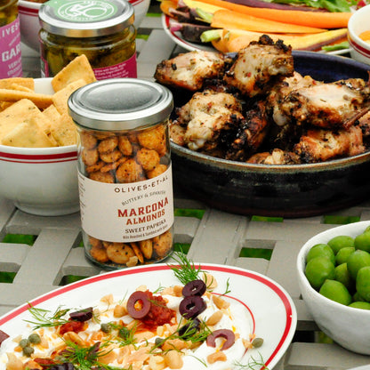 Assorted food items including a jar of Marcona Almonds, a bowl of salad, and a plate of grilled chicken on a table.