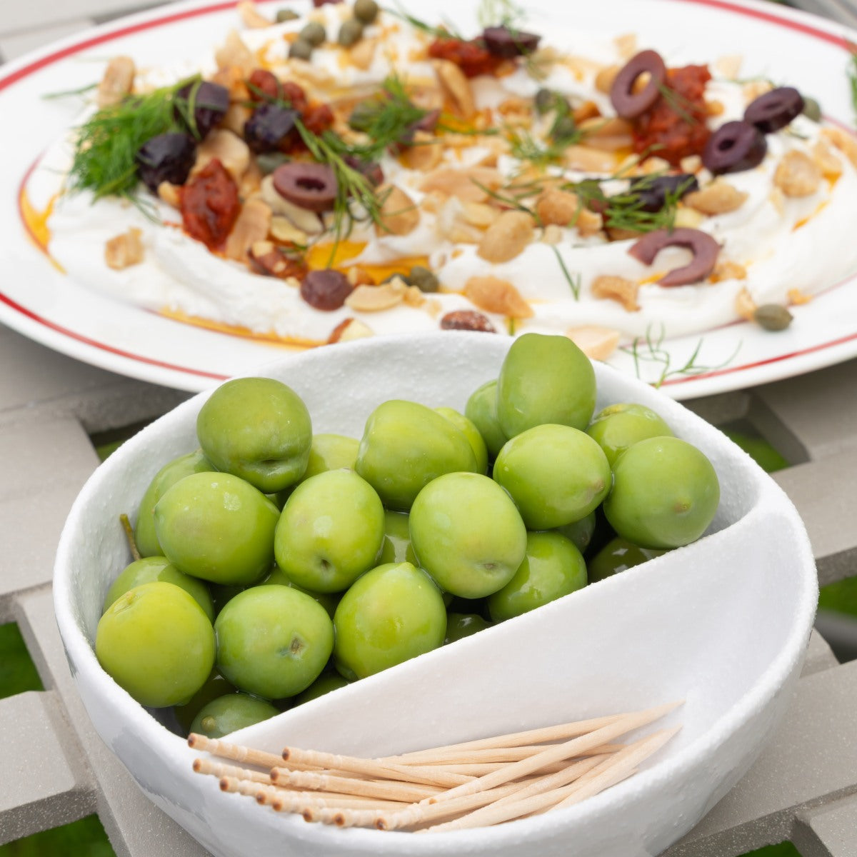 Bowl of Nocellara olives with a plate of labneh in the background