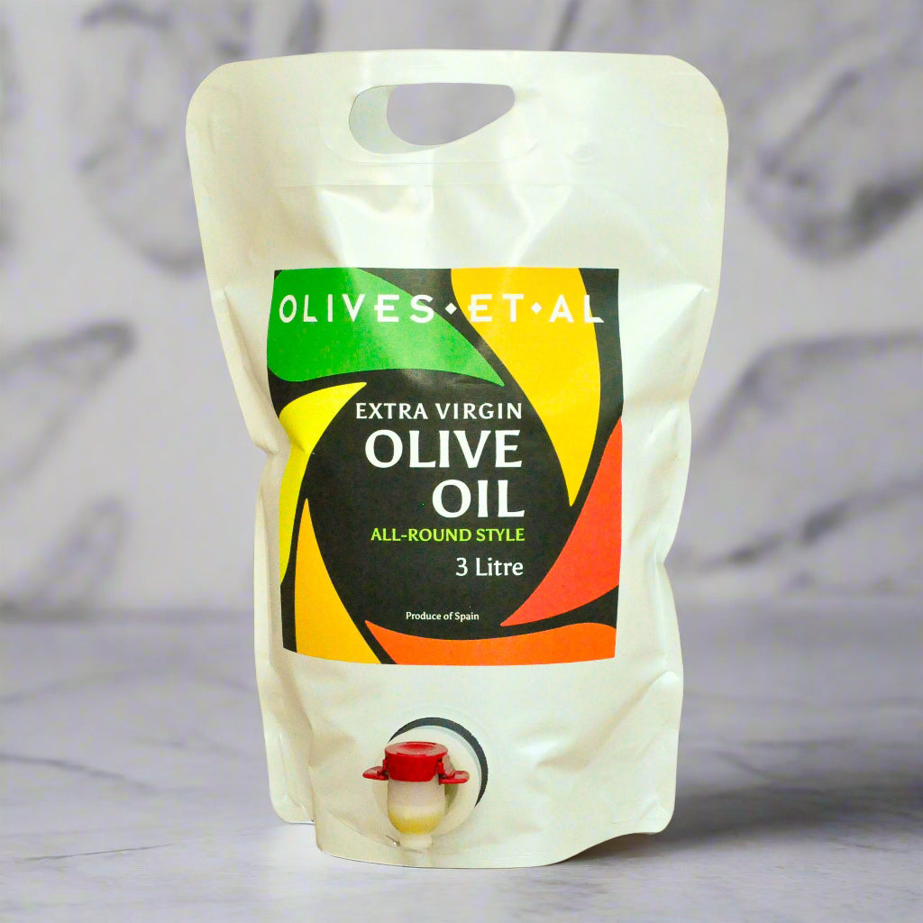 Pouch of extra virgin olive oil with a colorful label on a wooden surface.