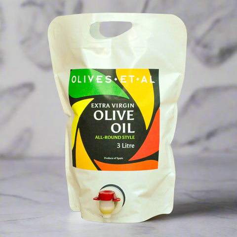 Pouch of extra virgin olive oil with a colorful label on a wooden surface.