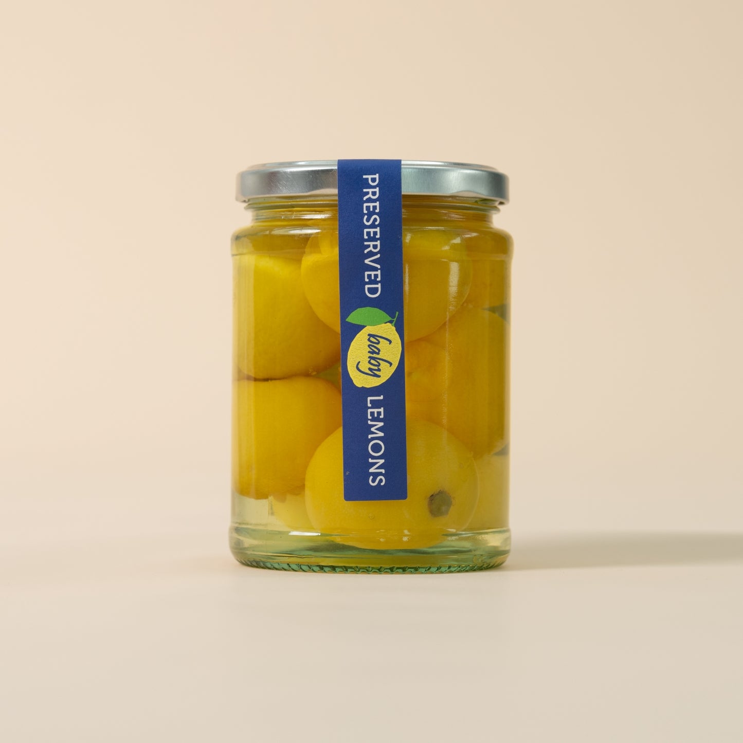 A glass jar of preserved lemons with a blue and yellow label, set against a solid beige background.