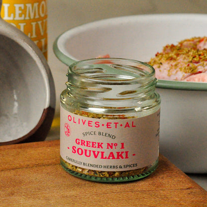 Jar of 'Greek No. 1 Souvlaki' spice blend by Olives Et Al on a wooden surface with a blurred background.