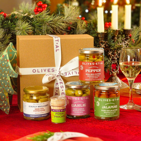 Gift box with Olives Et Al jars on a festive table with candles and greenery.