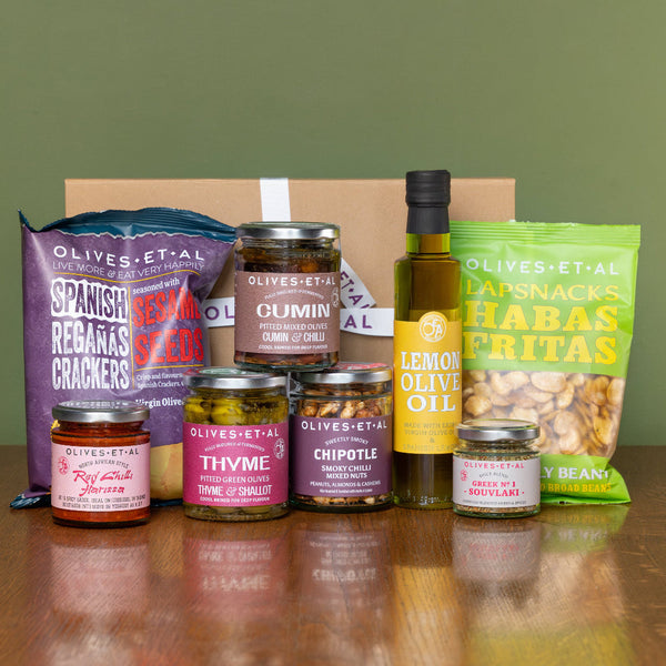 Assorted Olives Et Al food products including olive jars, a bottle of lemon olive oil and bags on a wooden surface with Habas Fritas and Reganas. 