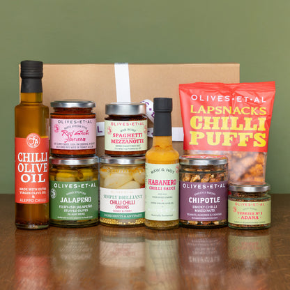 Collection of Olives & Al snacks including oils, sauces, and puffs on a reflective surface with a green background.