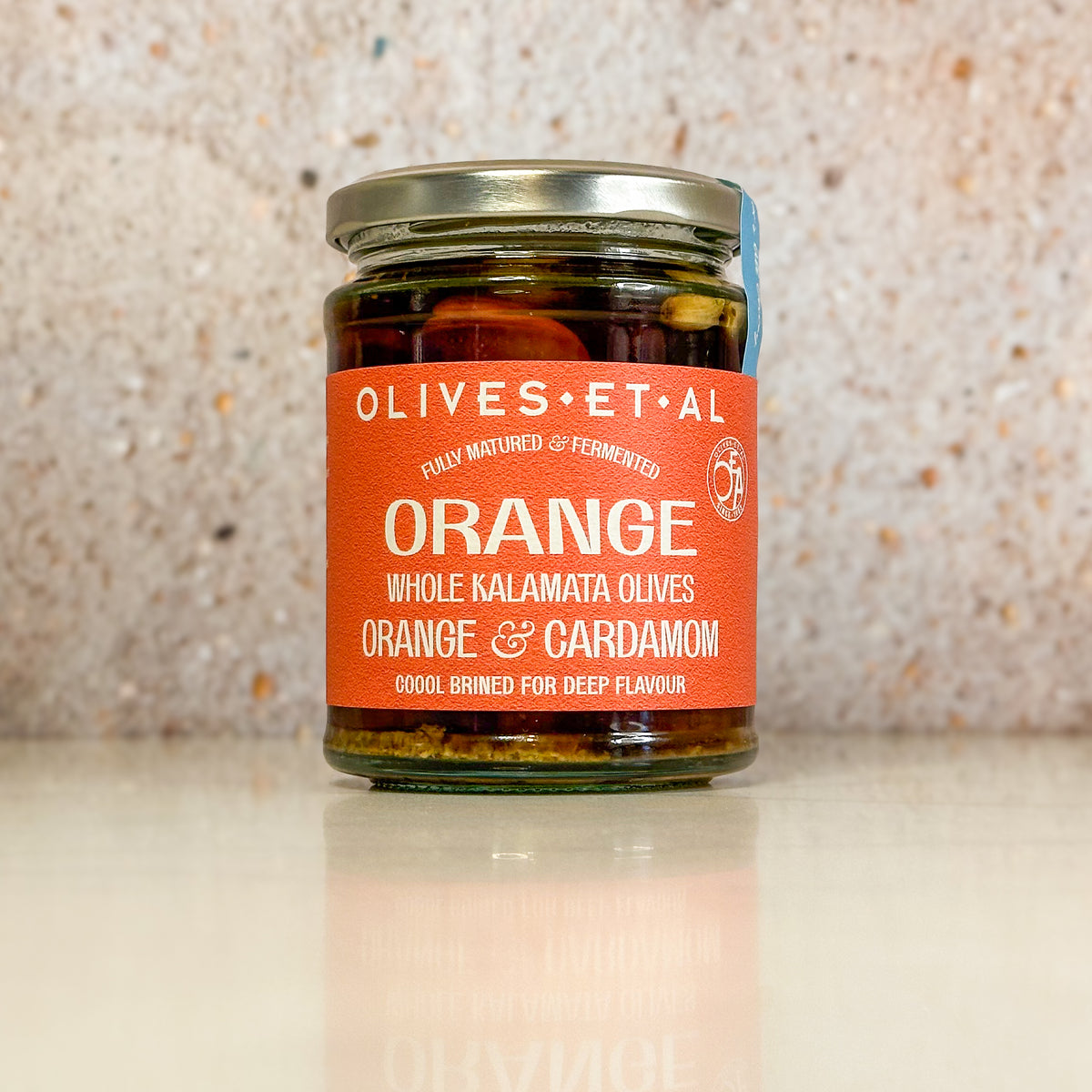 Jar of Orange & Cardamom whole Kalamata olives on a pale stone surface
