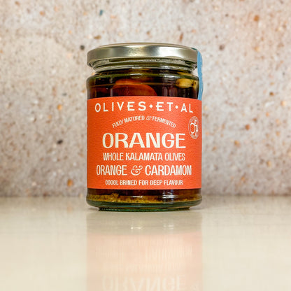 Jar of Orange & Cardamom whole Kalamata olives on a pale stone surface