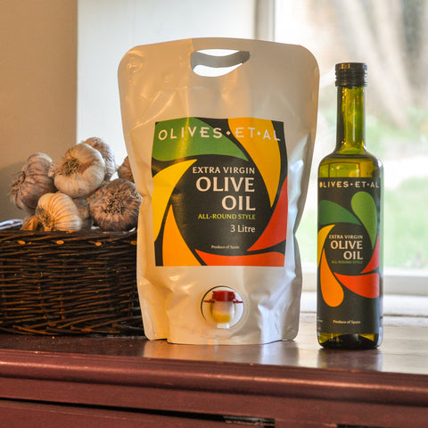 OLIVES ET AL olive oil packaging and bottle on a wooden surface with garlic in the background