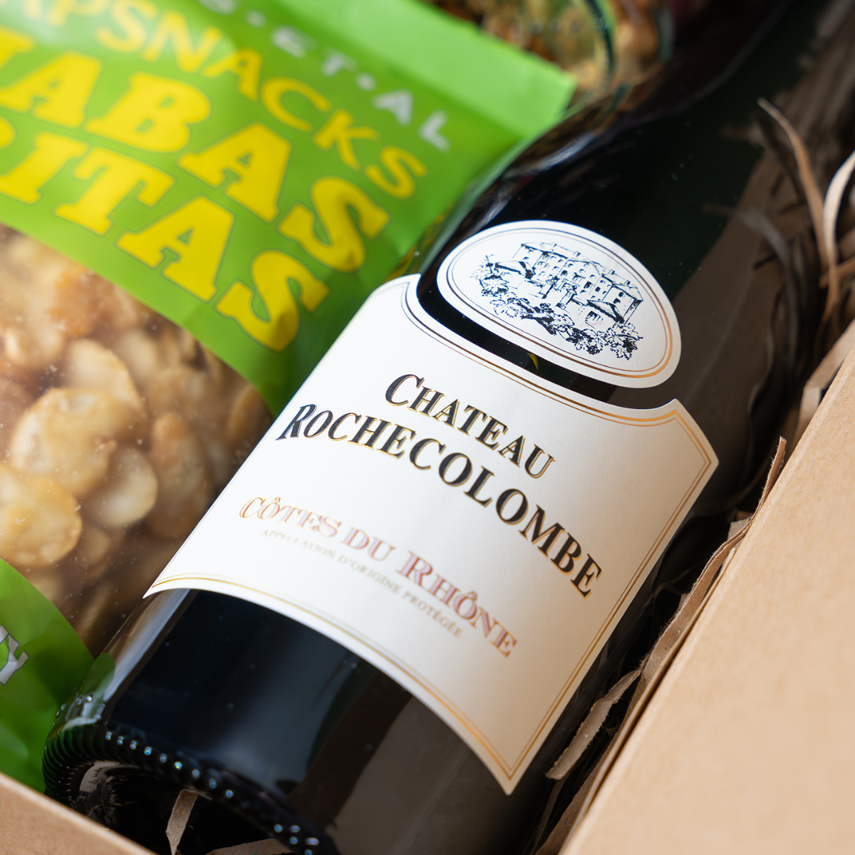 Bottle of Chateau Rochecolombe wine with a box of snacks in the background