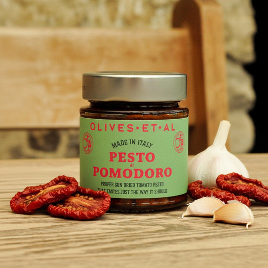 Jar of Olives Et Al Pesto di Pomodoro on a wooden surface with dried tomatoes and garlic.