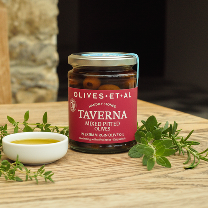 Jar of Olives et al Taverna olives on a wooden table with herbs and olive oil.